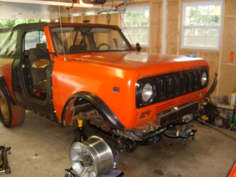 1994 Ford Bronco - An orange and black SUV, possibly an International Harvester Scout, is shown in a garage with its soft top removed.