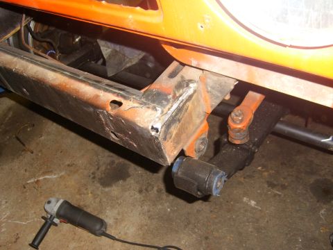 1994 Ford Bronco - Close-up of the rusty frame of an orange 1994 Ford Bronco, with a grinder visible on the floor.