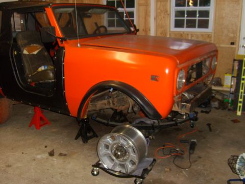 1994 Ford Bronco - This orange and black SUV is undergoing maintenance, with the front end elevated on jack stands and a wheel removed.