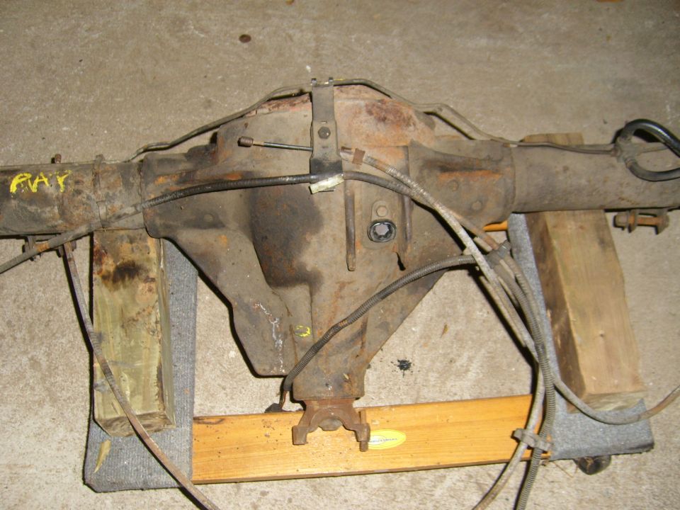 Rusty rear axle assembly on wooden supports. Yellow markings visible