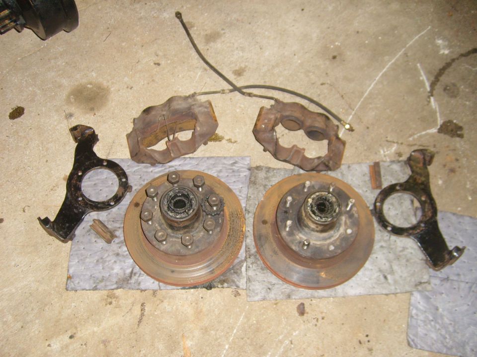 Two brake rotors with hubs, two brake calipers, and two steering knuckles laid out on a concrete floor