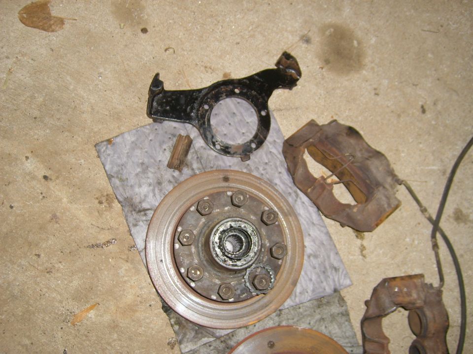 Disassembled brake rotor, caliper, and mounting bracket on a concrete floor