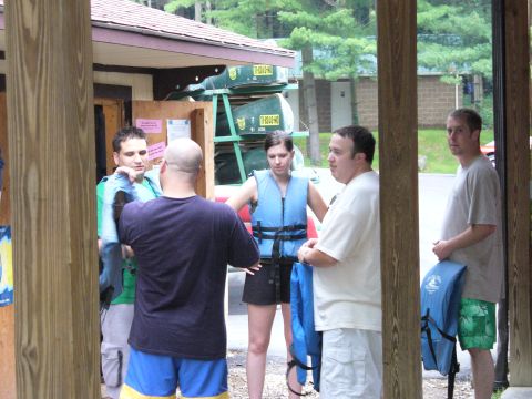 1991 Ford Probe - People in life vests stand near a building with canoes stacked on racks, suggesting an outdoor recreational activity.