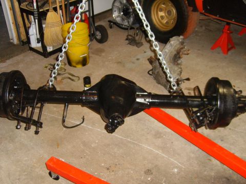 1994 Ford Bronco - A black rear axle assembly, likely from a truck or SUV, is suspended by chains in a garage setting.