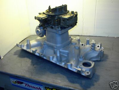 1979 Ford Bronco - Silver intake manifold with a carburetor mounted on top, displayed on a table.