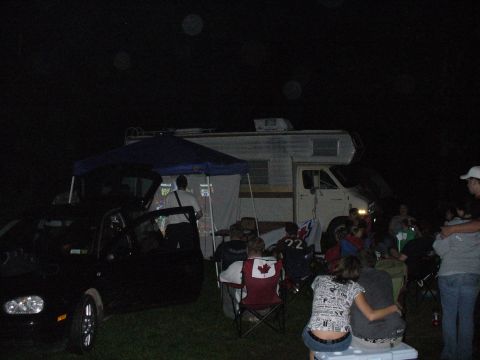 1991 Ford Probe - A group of people are socializing outdoors at night, with an RV and a car present.