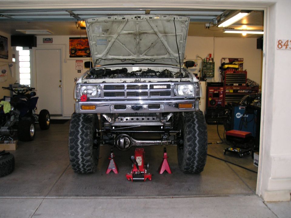 White Toyota pickup front view in garage, hood up, solid front axle swap over red jack stands