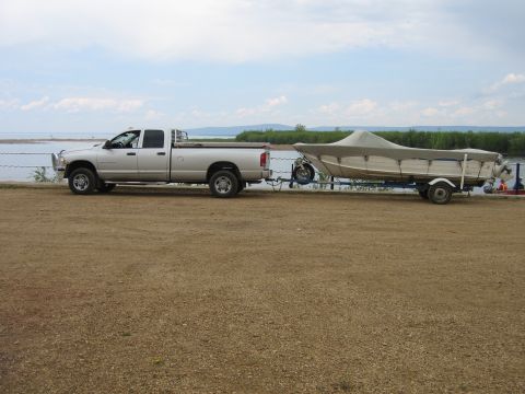 2005 Dodge 3500 - Silver Dodge 3500 pickup truck is seen from the side towing a boat on a trailer near a large body of water.