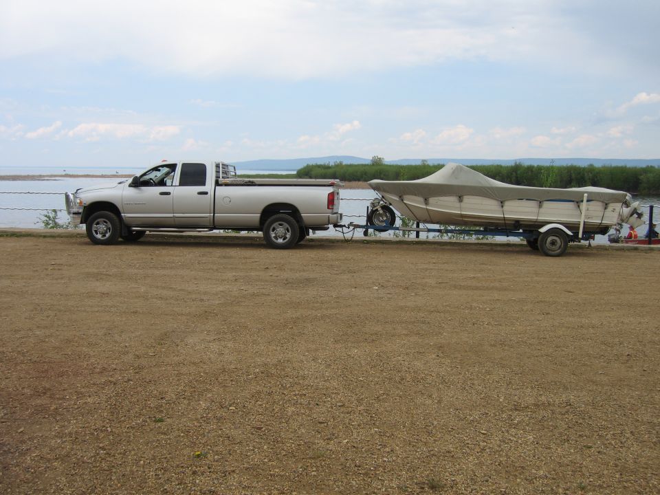 2005 Dodge 3500 pickup truck towing a covered boat on a trailer by a body of water