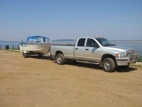2005 Dodge 3500 - A silver 2005 Dodge 3500 pickup truck is parked on a dirt lot, towing a boat on a trailer.
