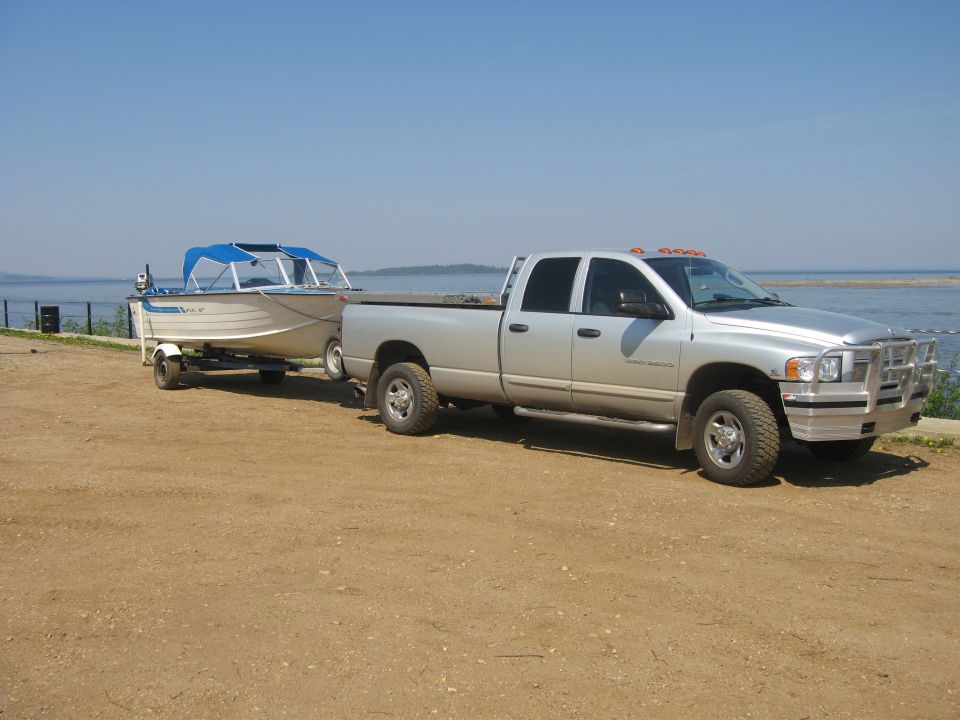 Silver Dodge Ram pickup truck towing a boat on a trailer near a body of water