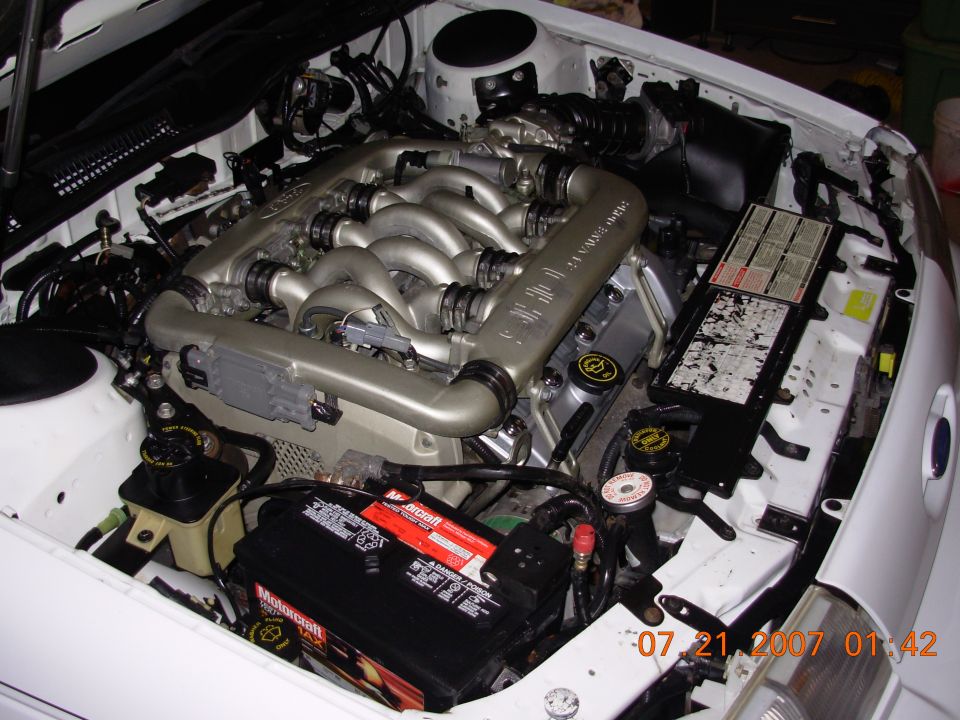 Engine bay with V-shaped engine, battery, and various hoses and components