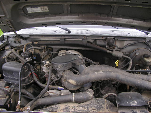 Engine bay with hoses, wires, and engine components visible. Text on a hose reads 'CAUTION FAN'