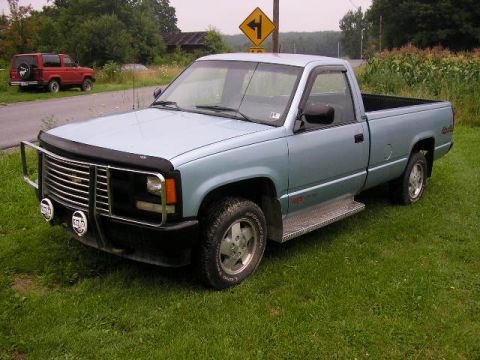 1994 Ford Probe - A light blue pickup truck is parked on a grassy area next to a road, with a red SUV visible in the distance.