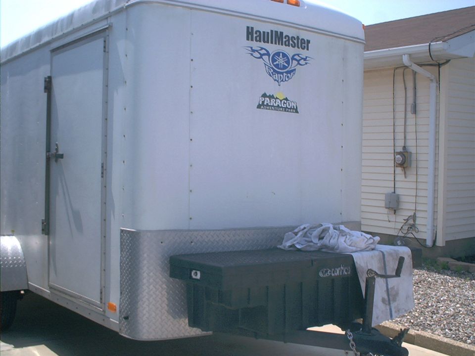 Rear view of a white enclosed cargo trailer with a black toolbox mounted on the tongue
