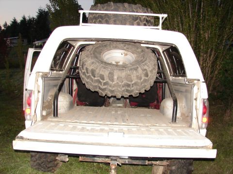 1996 Ford Bronco - Rear view of a white 1996 Ford Bronco, modified with a spare tire inside and on the roof rack, and an aftermarket roll cage.