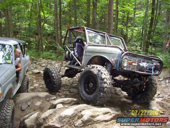 Modified 1974 Ford Bronco with roll cage and large tires on rocky terrain