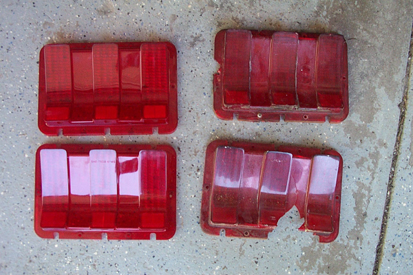 Four red car tail light lenses, two intact and two damaged, lie on a concrete surface
