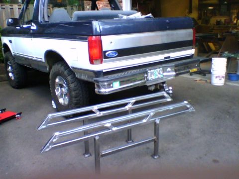 1993 Ford Bronco - A two-tone Ford Bronco is parked in a garage with custom sliders displayed nearby.