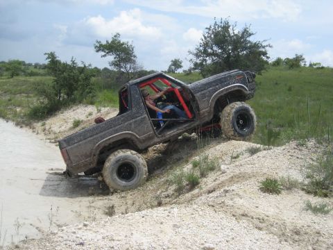 1986 Ford Bronco - This modified off-road vehicle navigates a challenging dirt incline under a cloudy sky.