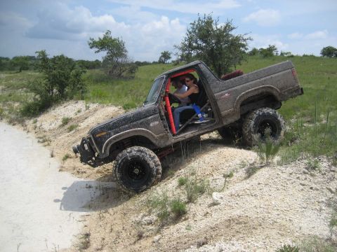 1986 Ford Bronco - A 1986 Ford Bronco navigates a challenging off-road terrain with two occupants inside.