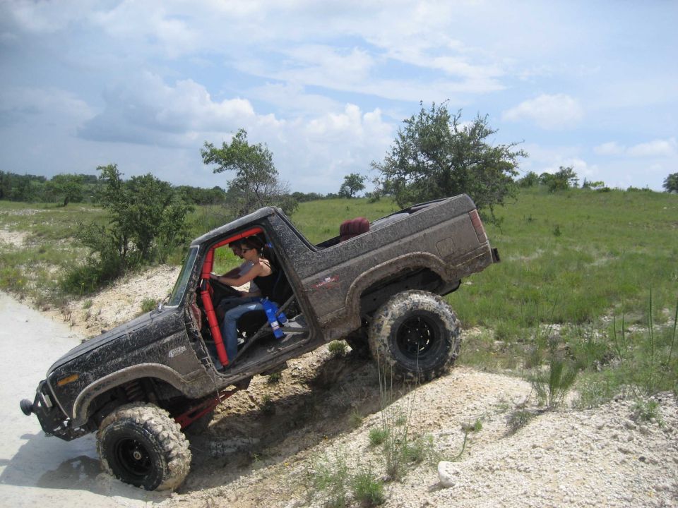 Modified Ford Bronco with roll cage and large tires climbing a dirt hill