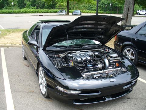 1991 Ford Probe - A black Ford Probe is parked with its hood open, revealing the engine bay and part of another vehicle to its right.