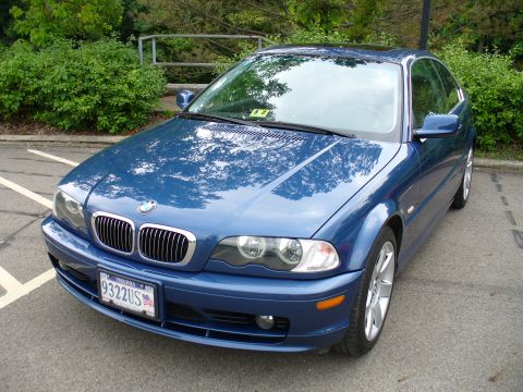 1991 Ford Probe - This blue BMW coupe is parked in a lot, with trees and bushes in the background.