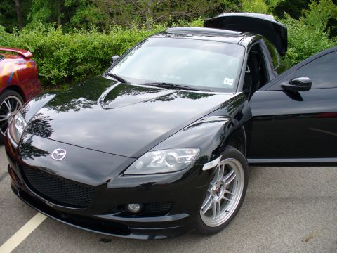 1991 Ford Probe - A black Mazda RX-8 is parked with its driver's door and trunk open, next to another vehicle.