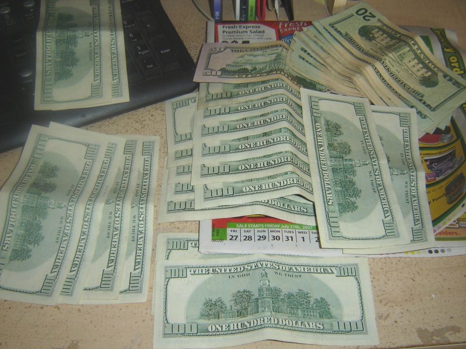 Stacks of US hundred dollar bills and some twenty dollar bills on a desk with a calendar and keyboard