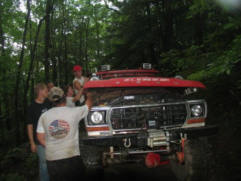 1995 Ford C-350 (Centurion Conversions) - A group of people are gathered around the engine of a red off-road truck, which is parked in a forest.
