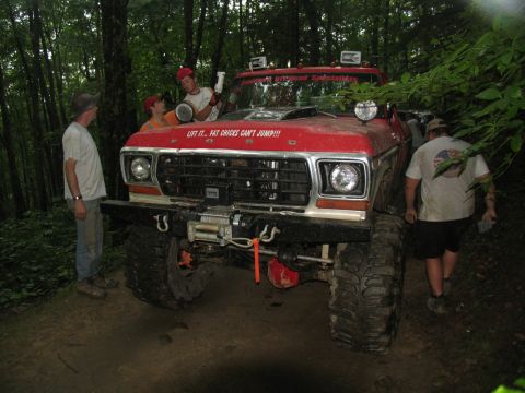 1995 Ford C-350 (Centurion Conversions) - A heavily modified red Ford truck sits in a wooded area with several people nearby.