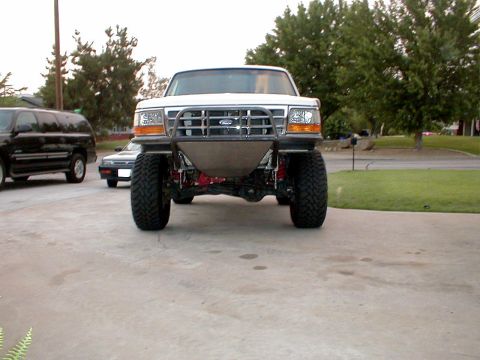 1996 Ford Bronco - A modified white Ford Bronco is parked on a driveway, showing its custom front bumper and off-road tires.