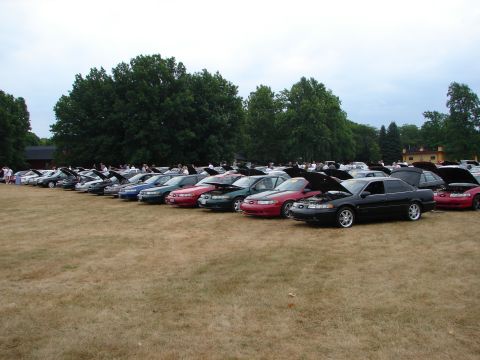 1993 Ford Taurus - Multiple sedans are parked in a field with their hoods open under an overcast sky.