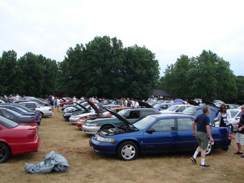 1993 Ford Taurus - Several cars are displayed with their hoods up at a car show on a cloudy day.