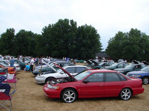 1993 Ford Taurus - A red sedan is parked at an outdoor car show with many other vehicles.