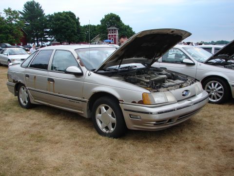 1993 Ford Taurus - A silver sedan with its hood open sits on dry grass at an outdoor event.