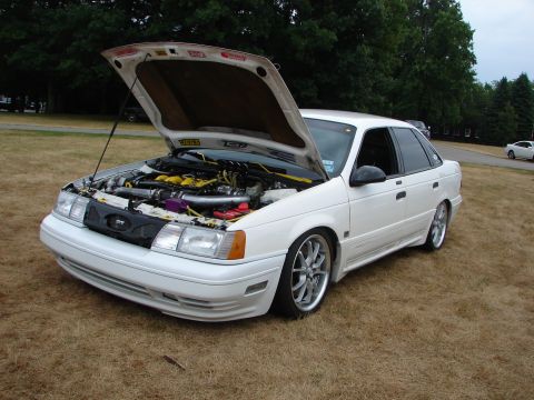 1993 Ford Taurus - A white 1993 Ford Taurus is parked on dry grass with its hood open, revealing a modified engine bay.