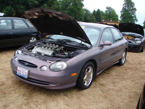 1993 Ford Taurus - A purple Ford Taurus SHO is displayed with its hood open, revealing the engine, while other vehicles are parked nearby.