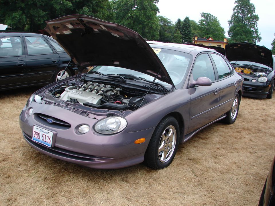 Purple Ford Taurus SHO with hood open, showing V8 engine. Another car is parked behind it