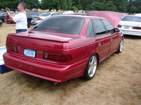 1993 Ford Taurus - A red sedan is parked on dry grass with other vehicles around it.