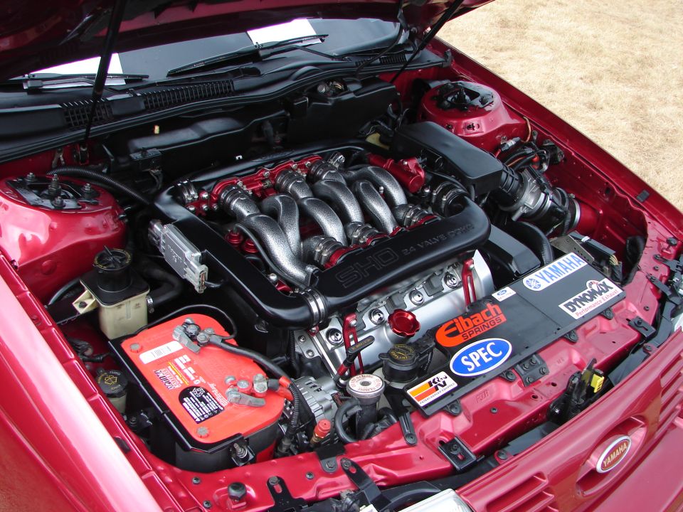 Red 1993 Ford Taurus SHO engine bay with a V8 engine, custom intake, and various performance stickers