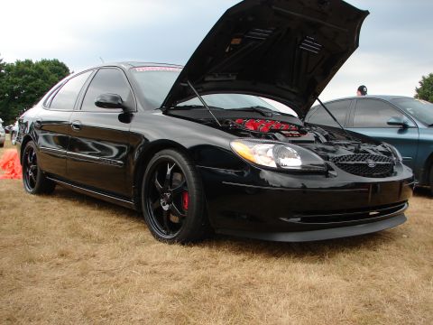 1993 Ford Taurus - Black sedan with hood open, parked on dry grass next to another vehicle.