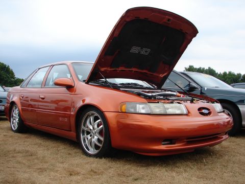 1993 Ford Taurus - Orange 1993 Ford Taurus SHO at a car show, hood open, revealing engine details.