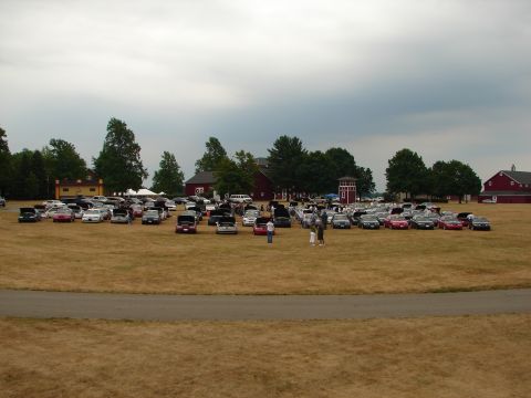 1993 Ford Taurus - A large gathering of cars are parked on a field, with several people milling about.
