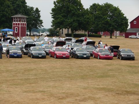 1993 Ford Taurus - Multiple Ford Tauruses are gathered on a grassy field, some with hoods open, under a cloudy sky.