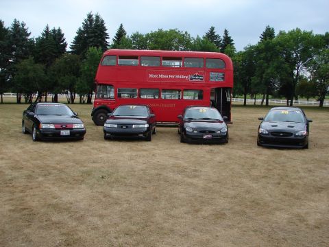 1993 Ford Taurus - Four Ford Taurus sedans, likely from the 1993 model year, are lined up in front of a vintage red double-decker bus.