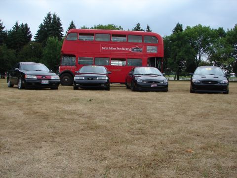 1993 Ford Taurus - Four Ford Taurus sedans are lined up in front of a red double-decker bus on a cloudy day.