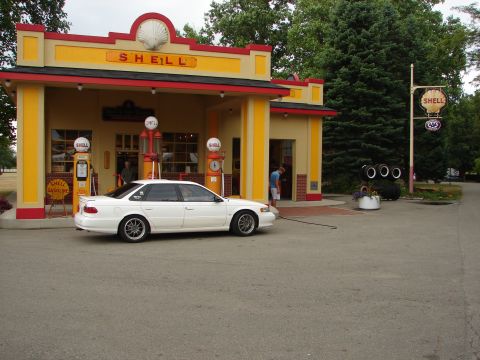 1993 Ford Taurus - A white sedan is parked next to a vintage Shell gas station with old-fashioned pumps.