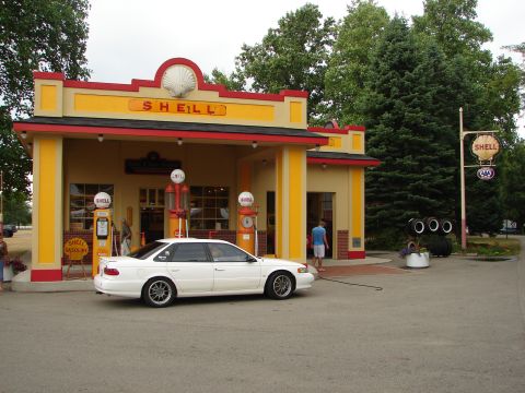 1993 Ford Taurus - A white sedan is parked at a vintage Shell gas station with old-fashioned gas pumps.